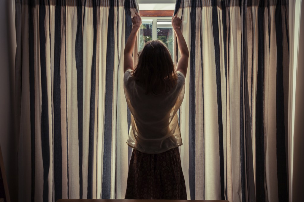 Young woman opening the curtains at sunrise